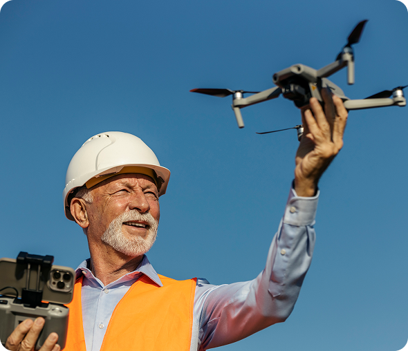 Senior male environmentalist in orange vest operating drone outdoors under clear blue sky